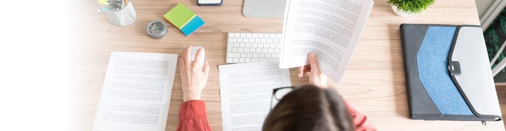 Brunette woman sitting at a desk reading text and clicking the mouse