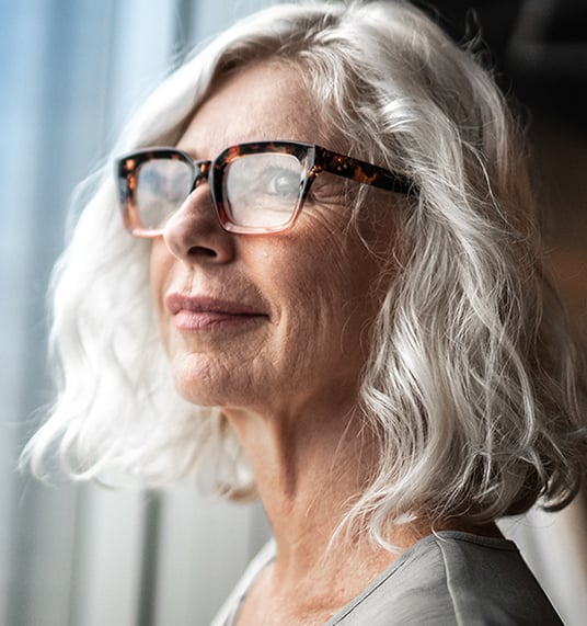 A gray-haired woman in glasses looks out the window