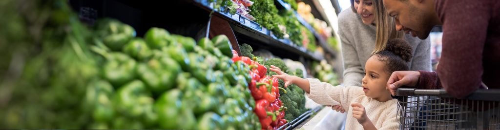 Child picking veg at supermarket with parents