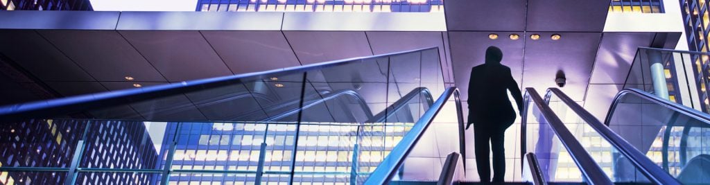 Silhouette of person walking up escalator in office building