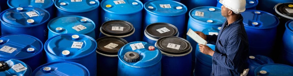 Man with clipboard looking over oil barrels